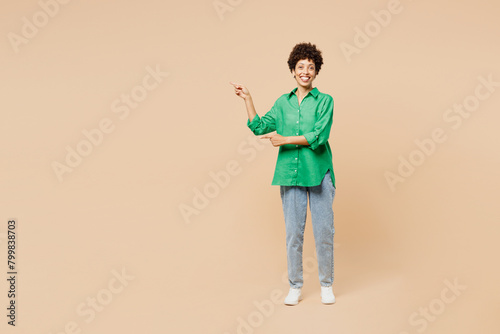 Full body young woman of African American ethnicity wear green shirt casual clothes point index finger aside indicate on area isolated on plain pastel light beige background studio. Lifestyle concept.