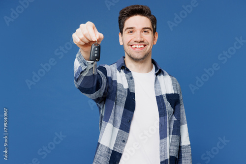 Young smiling happy man wear shirt white t-shirt casual clothes hold in hand car key fob keyless system stretch arm to camera isolated on plain blue cyan background studio portrait. Lifestyle concept.