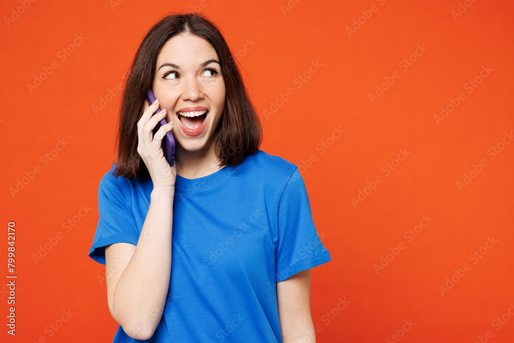 Young surprised shocked excited happy woman wear blue t-shirt casual clothes talk speak on mobile cell phone conducting pleasant conversation isolated on plain red orange background Lifestyle concept Young surprised shocked excited happy woman wear blue t-shirt casual clothes talk speak on mobile cell phone conducting pleasant conversation isolated on plain red orange background Lifestyle concept