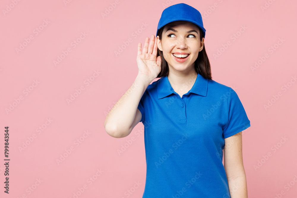Professional delivery girl employee woman wear blue cap t-shirt uniform workwear work as dealer courier try to hear you overhear listening intently isolated on plain pink background. Service concept.