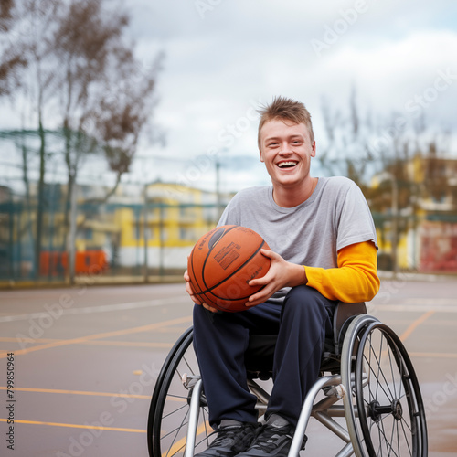 Determined and smiling disabled young man player in a wheelchair. Strong male boy smile at the camera sitting on a wheel chair alone in the basketball field with nobody playing in background