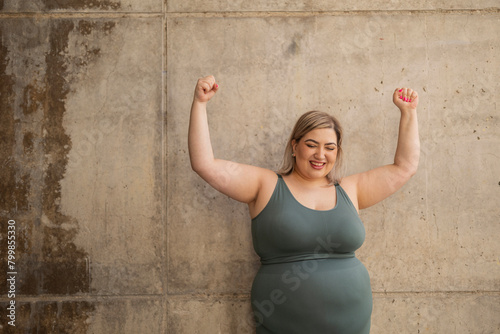 Cheerful curvy woman flexing muscles in front of wall photo