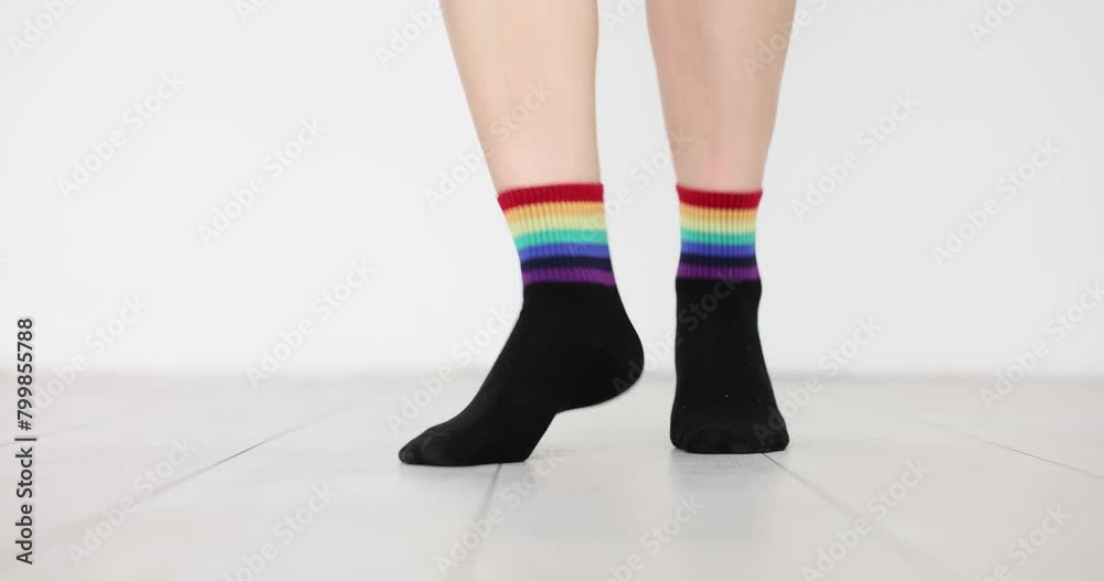 Stepping feet dressed in black socks with image of rainbow flag. Clothes with LGBTQ flag decor on white background. Support for vulnerable social groups Stepping feet dressed in black socks with image of rainbow flag. Clothes with LGBTQ flag decor on white background. Support for vulnerable social groups