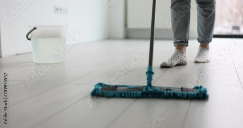 Woman cleans floor with mop in modern office at end of working day. Female in cotton socks supports workplace hygiene. Wet cleaning of dust and dirt