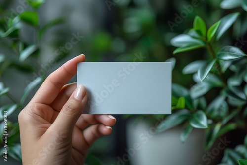 Close up shot of a blank white paper card mock up in a woman's hands. The girl holds and shows a blank card in front of her.