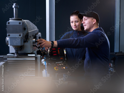Smiling engineer explaining CNC machine to trainee at factory