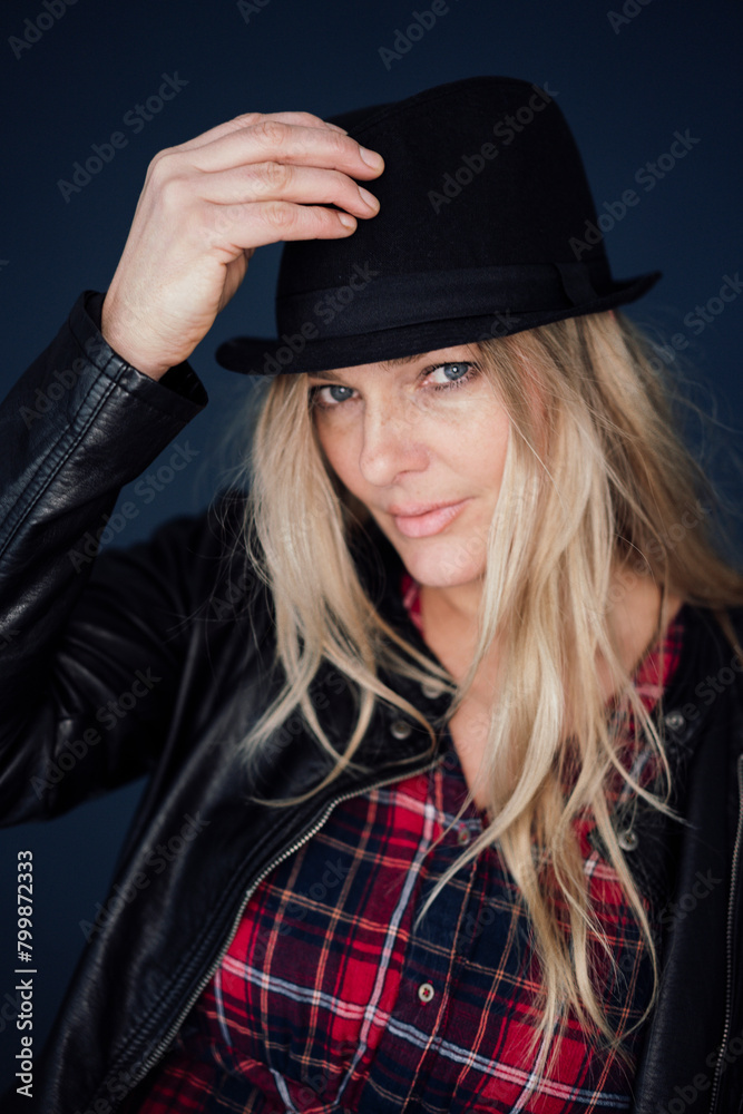 Blond mature woman wearing hat and jacket against colored background Blond mature woman wearing hat and jacket against colored background