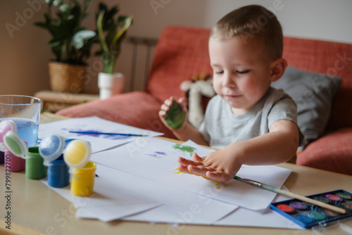 Boy making colored handprint on sheet of paper at home
