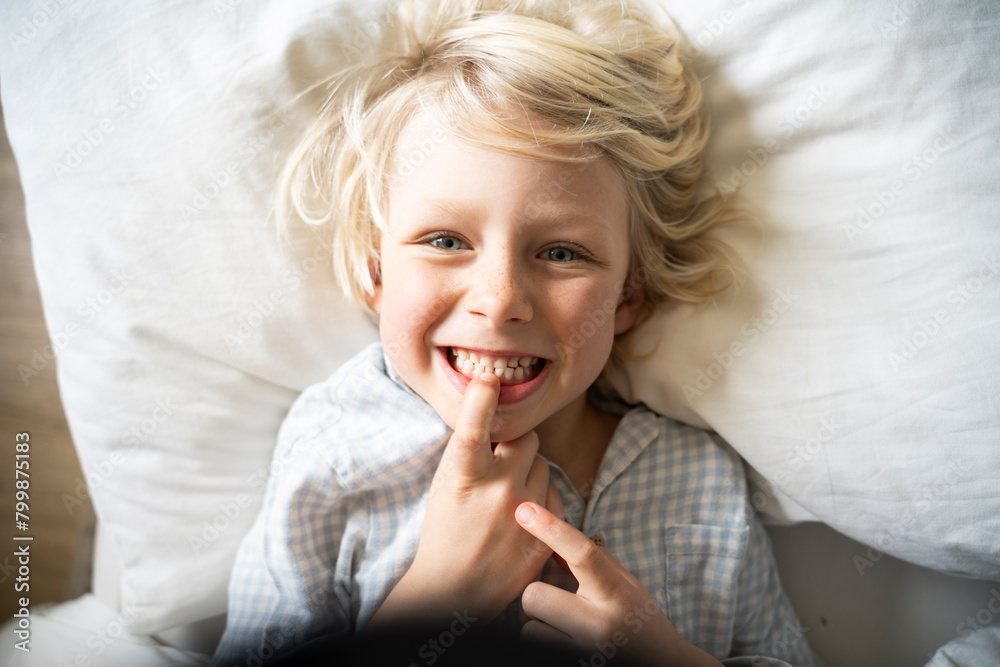 Happy boy touching and showing teeth on bed at home Happy boy touching and showing teeth on bed at home