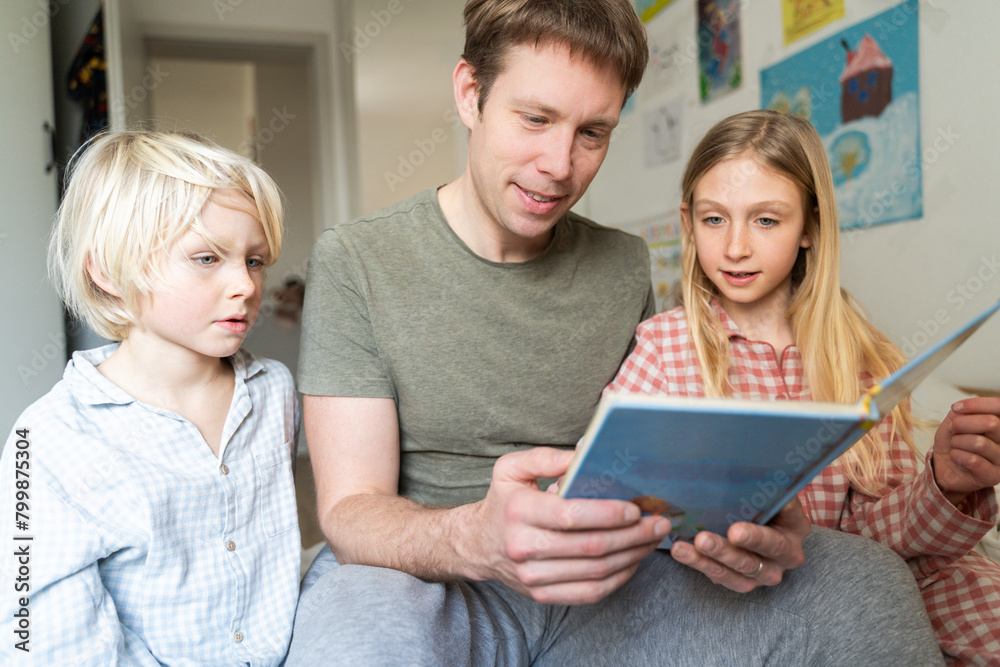 Smiling father reading book with children at home Smiling father reading book with children at home