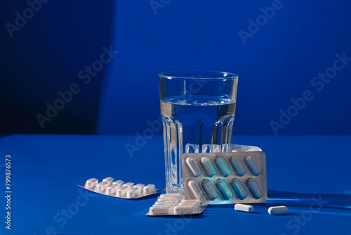 Glass of water with medicines on blue background