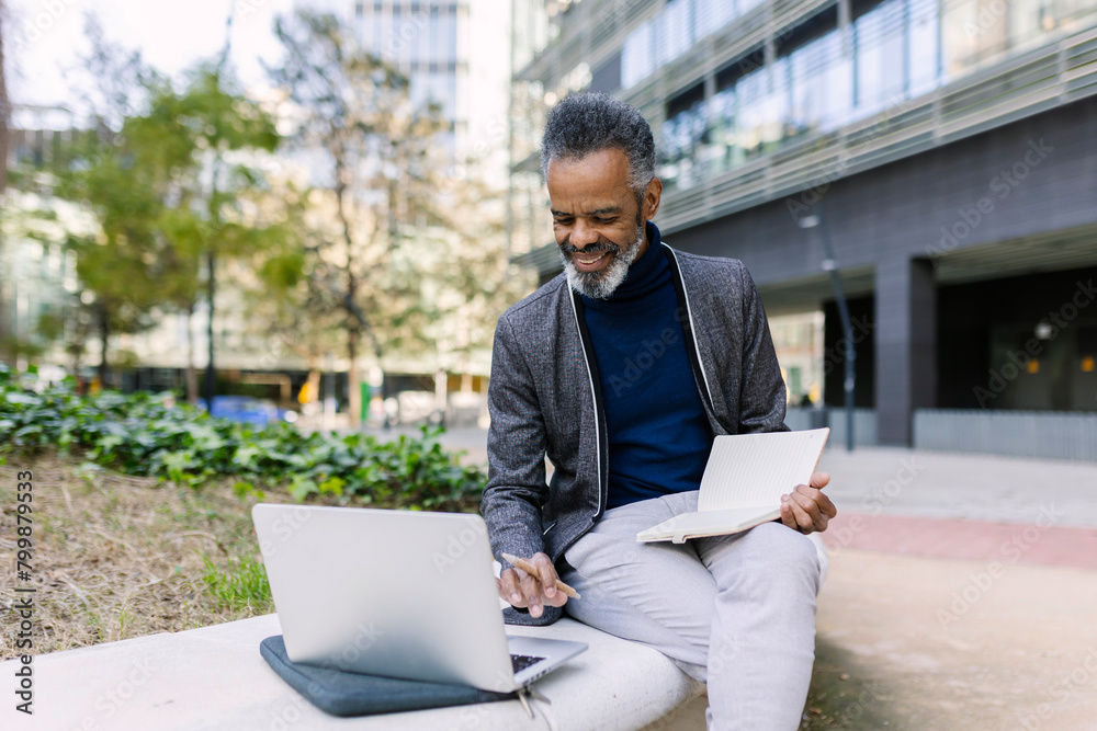 Smiling businessman sitting with diary and working on laptop Smiling businessman sitting with diary and working on laptop