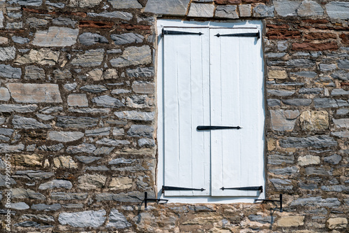 Colonial stone house exterior with closed white wooden window shutters and long antique hinges