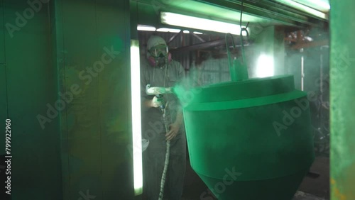 Industrial painting process in chamber at factory. Painter spraying green paint on detail in special booth. Technician in safety wear working at production. Master paint metal in specialised workshop photo
