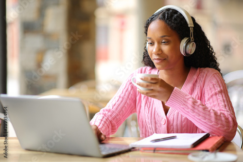 Black student studying using laptop and headpone in a bar