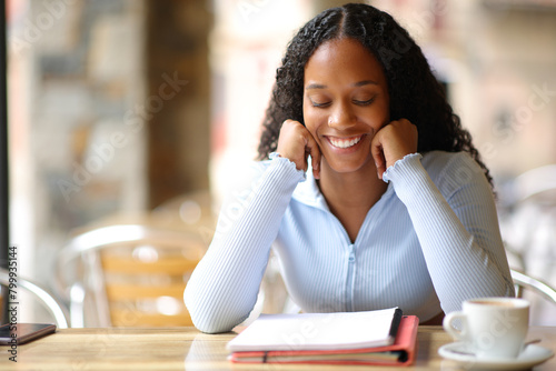 Happy black student memorizing notes in a bar terrace