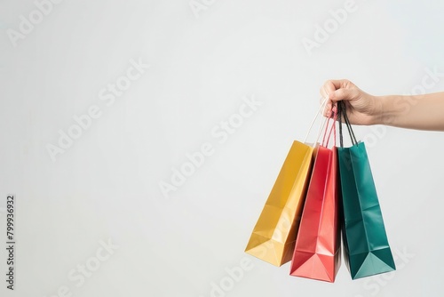 A hand holding multiple colourful shopping bags on a white background,