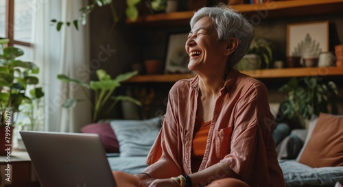 A cheerful mature woman is smiling while using a laptop in a cozy home environment filled with plants, suggesting a theme of comfort and modern connectivity.