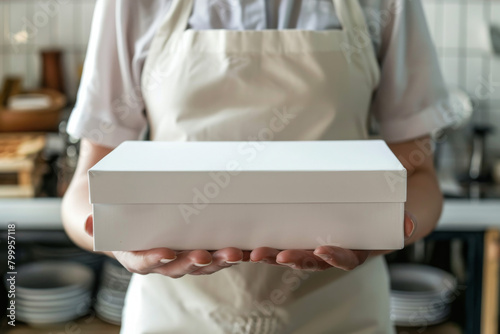 Chef holding a blank white pizza box in a kitchen