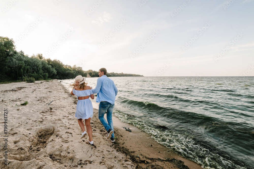 Man and woman running on sand sea and spending time together. Female and male run on beach enjoy summer day. Happy couple in love holding hands and looking at each other on seashore. Back view.