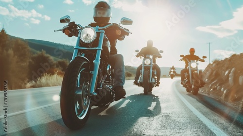 A group of motorcyclists riding on a sunny highway, with one rider leading the pack. photo