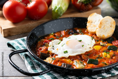 Vegetable pisto manchego with tomatoes, zucchini, peppers, onions,eggplant and egg, served in frying pan on wooden table