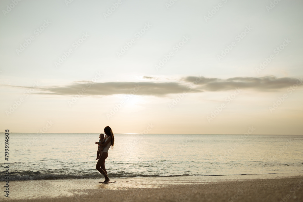 Young woman with her baby on the beach during sunset . Mother with her baby on the beach watching the sunset, copy space