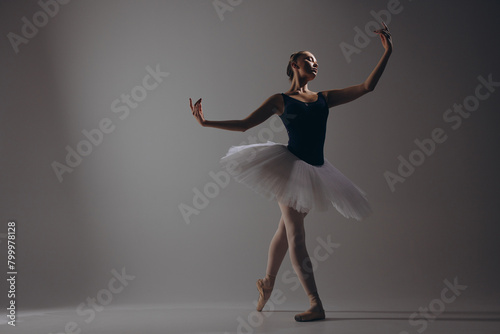Young ballerina in elegance white tutu and pointe shoes dancing against dark background. photo