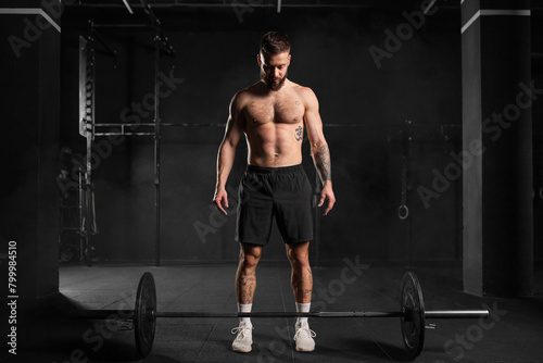 Strong man preparing for barbell lift, overhead squat, standing by barbell. Routine workout for physical and mental health.