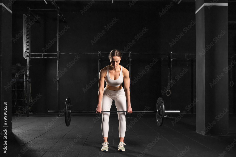 Woman performing deadlift as strength exercise. Lifting barbell off the ground. Routine workout for physical and mental health.
