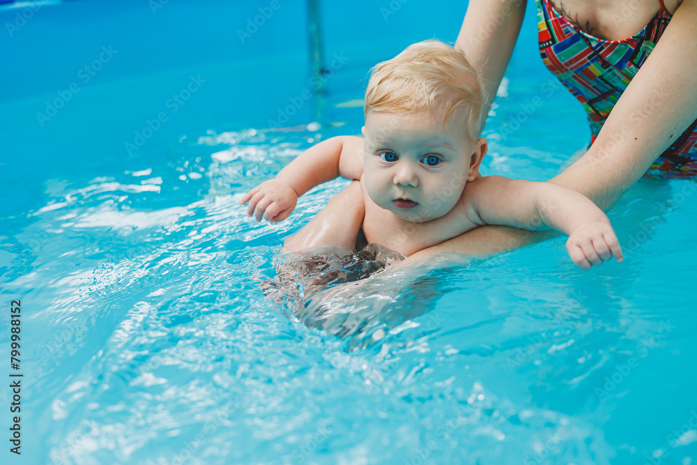 A baby learns to swim with a coach in the pool. Swimming pool for babies.