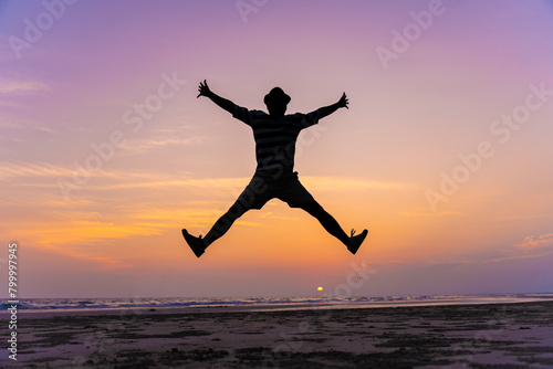 Happy young man jumping with outstretched arms on the beach with copy space. Beach silhouette background. Carefree and freedom concept on vacation.