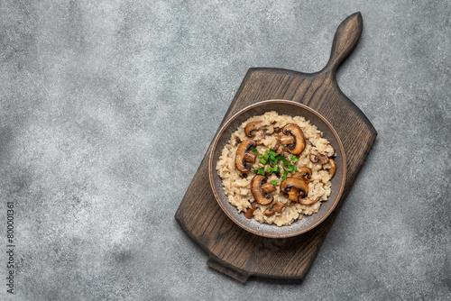 Risotto with mushrooms in a bowl on a wooden board, gray concrete background. Top view, flat lay, copy space.