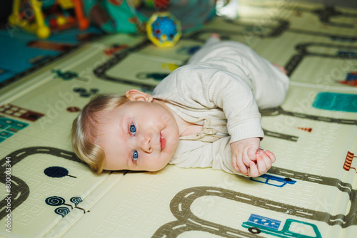 Photo of a 7-9 month old baby at home. A smiling child lies on the floor and plays with toys. Cute boy sitting on the floor.