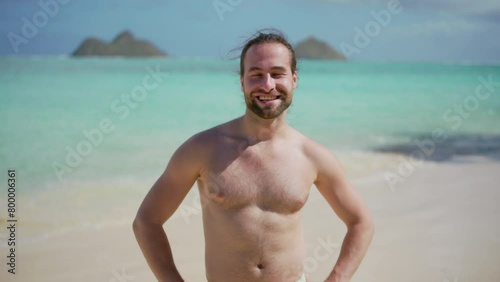 With a radiant smile that lights up the beach, a man enjoys the simple joys of a sunny day on the Hawaiian shores, with the picturesque Mokulua islands enhancing the tropical scenery. Slow motion.  photo