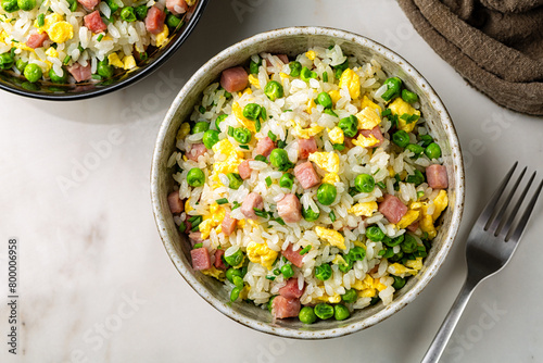 Billede på lærred Top view of cantonese Fried Rice and egg omelette with green pea, ham steak, spring onion, ribe long rice in a beige bowl on a white marble table, served with fork