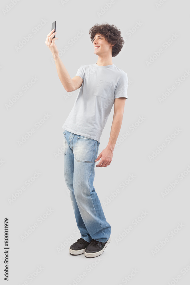 Young happy smiling handsome man using his smartphone, taking a selfie isolated against a gray background, full body image Young happy smiling handsome man using his smartphone, taking a selfie isolated against a gray background, full body image