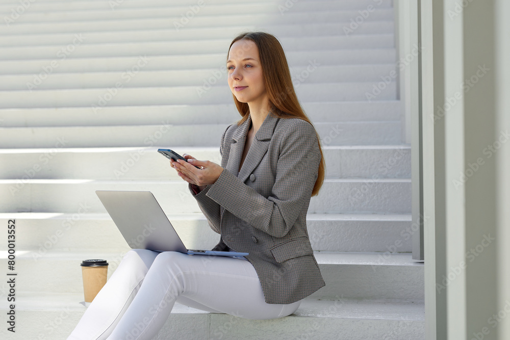 An attractive and stylish young woman is sitting on the steps in a city park and working on a laptop. The life of a freelancer An attractive and stylish young woman is sitting on the steps in a city park and working on a laptop. The life of a freelancer