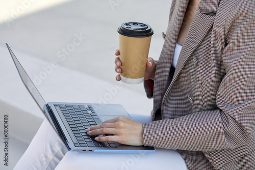 Successful businesswoman multitasks, savouring a hot beverage and working on her laptop in a serene outdoor setting photo