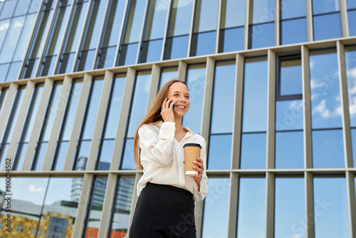 A business woman with a smile is talking on the phone and drinking coffee outside. Professional approach to business