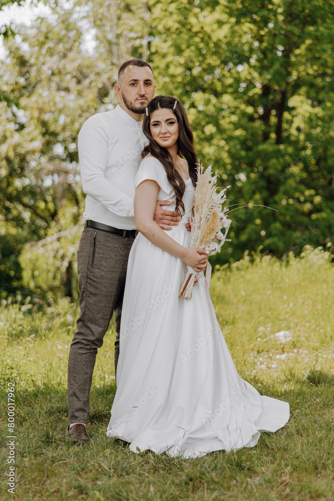 A bride and groom are posing for a picture in a grassy field