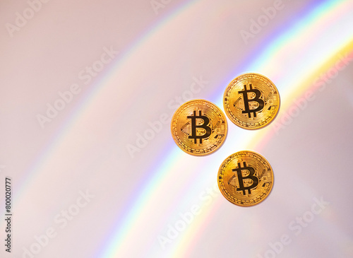 Gold bitcoins on a white background with a rainbow, copy space.