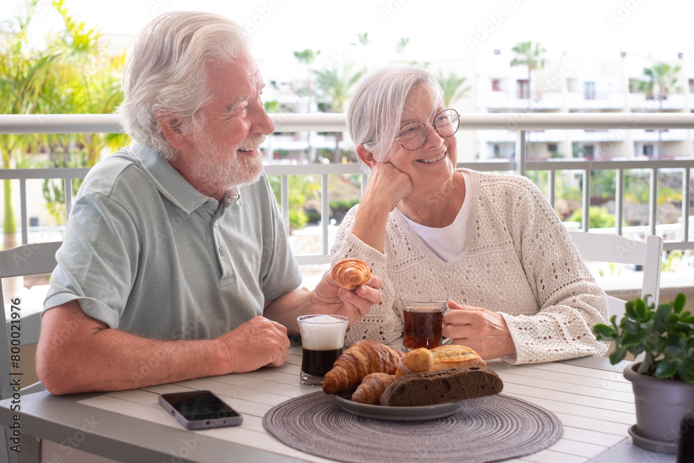 Smiling bonding senior retired couple enjoy breakfast together sitting outdoors on home terrace. Serene retirement lifestyle concept Smiling bonding senior retired couple enjoy breakfast together sitting outdoors on home terrace. Serene retirement lifestyle concept
