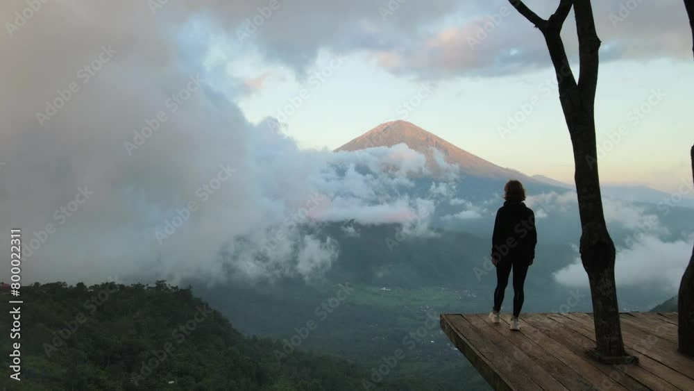 Silhouette of a young girl standing on a wooden platform high in the mountains, enjoying life, with a beautiful view of the clouds and the volcano mountain. Lahangan Sweet, Bali. Silhouette of a young girl standing on a wooden platform high in the mountains, enjoying life, with a beautiful view of the clouds and the volcano mountain. Lahangan Sweet, Bali.