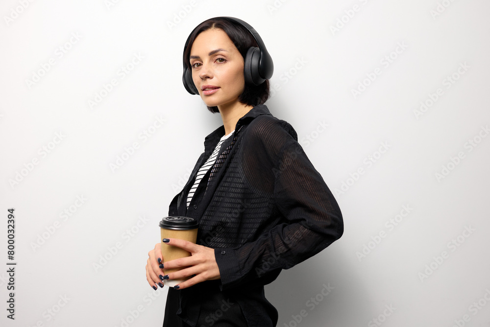 Stylish young woman in a fashionable look holds a cup of coffee and listens to music