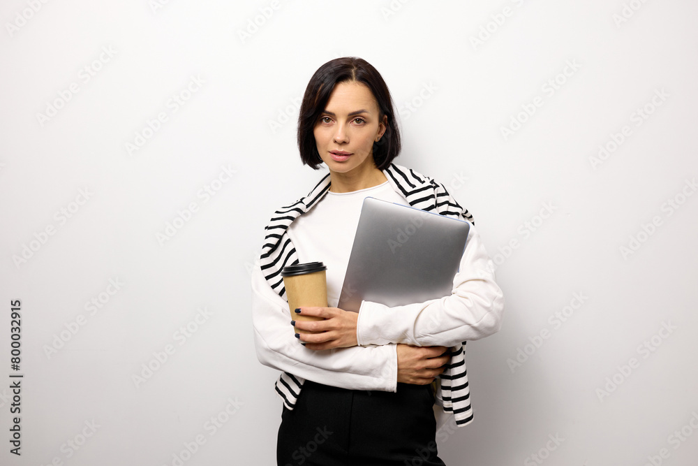 Confident business woman dressed in a white shirt holding a laptop and a cup of coffee during a break Confident business woman dressed in a white shirt holding a laptop and a cup of coffee during a break