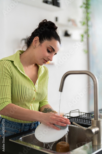 A serene woman in a vibrant green shirt carefully washes dishes at home, exhibiting a moment of domestic life