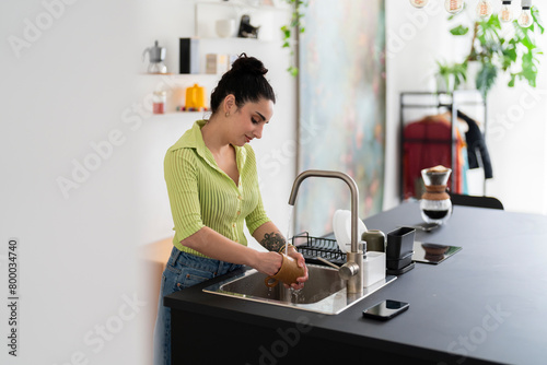 A serene woman in a vibrant green shirt carefully washes dishes at home, exhibiting a moment of domestic life photo