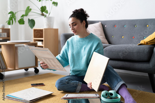 A young woman in a blue sweater examines a vinyl record, engaged in her passion for music, with a turntable and headphones nearby photo