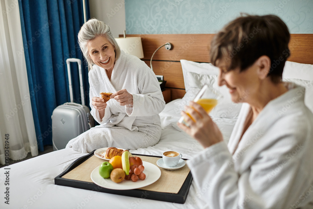 Two women, a loving senior lesbian couple, sitting tenderly intertwined on a bed. Two women, a loving senior lesbian couple, sitting tenderly intertwined on a bed.